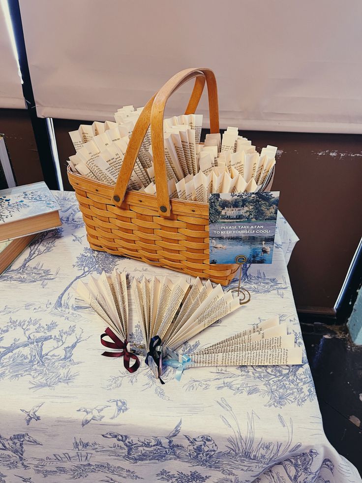 a table topped with books and a basket filled with folded paper fan next to an open book