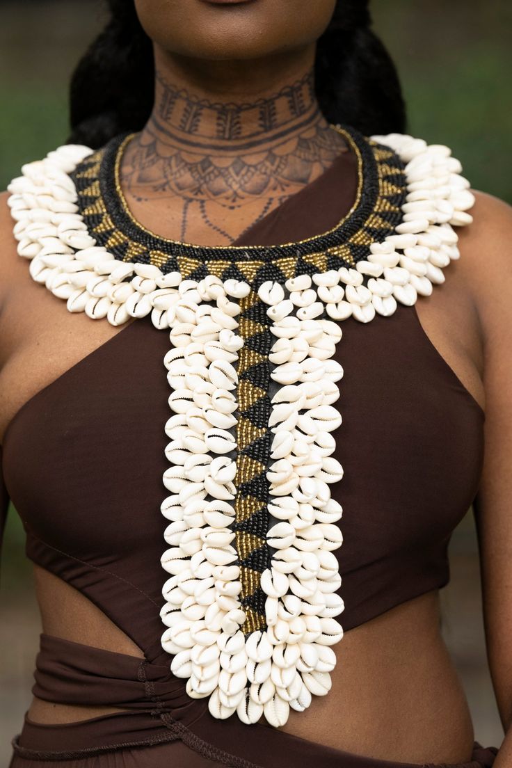 Discover the Bosaso Necklace, an exquisite accessory handmade in Africa. Adorned with over 150 lavish cowrie shells, this necklace exudes an opulent style to elevate any look. Perfect for creating an unforgettable statement, the Bosaso Necklace is sure to make a lasting impression. Large necklace material: cowrie shells, faux leather, string handmade& imported Shell Crowns, Baroque Period, Cowrie Shell Jewelry, African Princess, Cowrie Shell Necklace, African Royalty, African Accessories, Cowrie Shells, Fashion Sketches Dresses