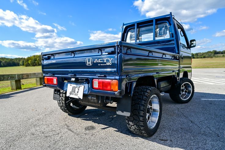 a blue pick up truck parked in a parking lot next to a fence and grass field