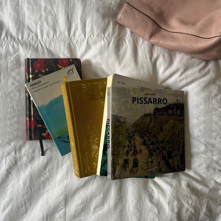 three books sitting on top of a white bed next to each other in front of a pink pillow