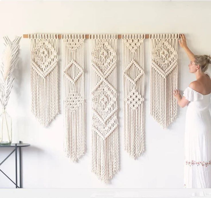 a woman standing next to a wall hanging with macrame beads