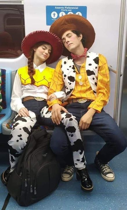 two people dressed in costumes sitting on a subway train together, one wearing a cowboy hat and the other as a cowgirl