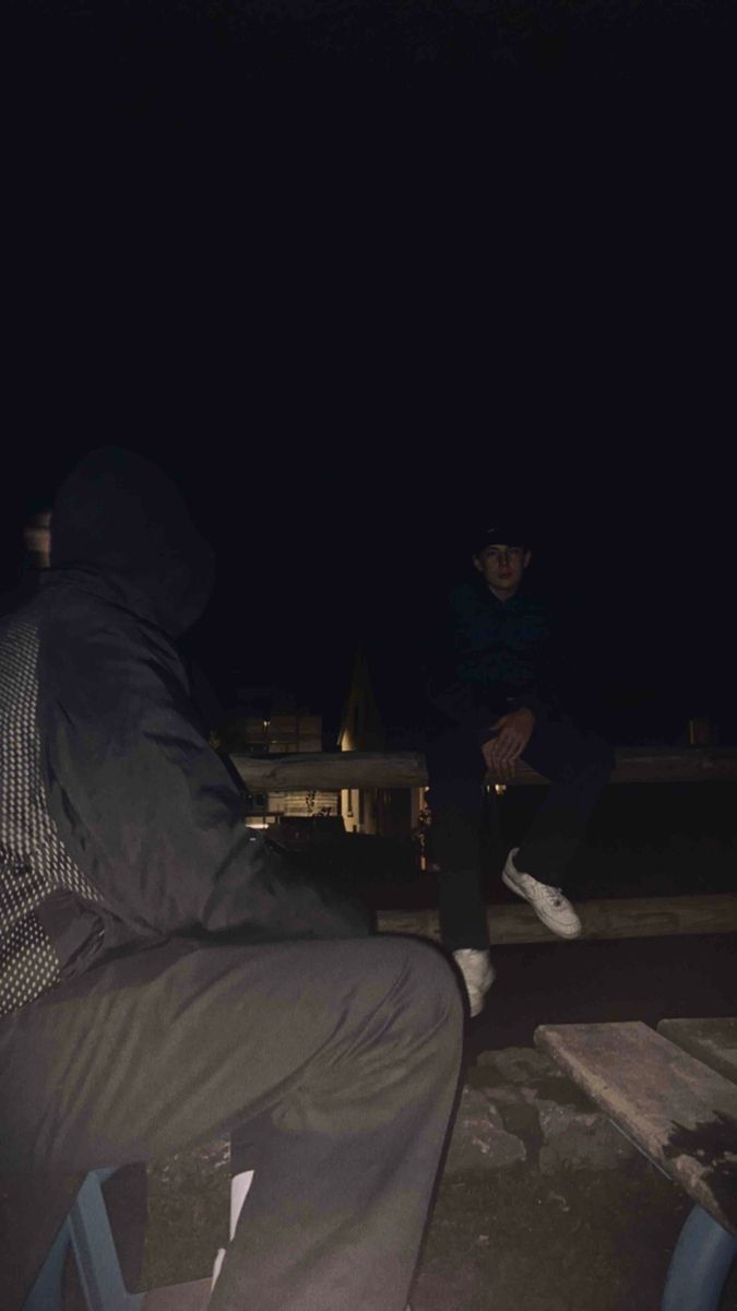 a man sitting on top of a bench at night with his feet up in the air