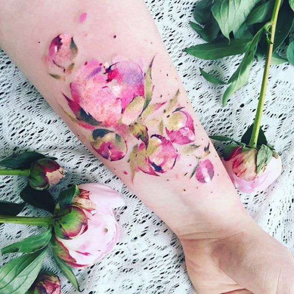 a woman's arm with pink flowers on it and green leaves around the wrist