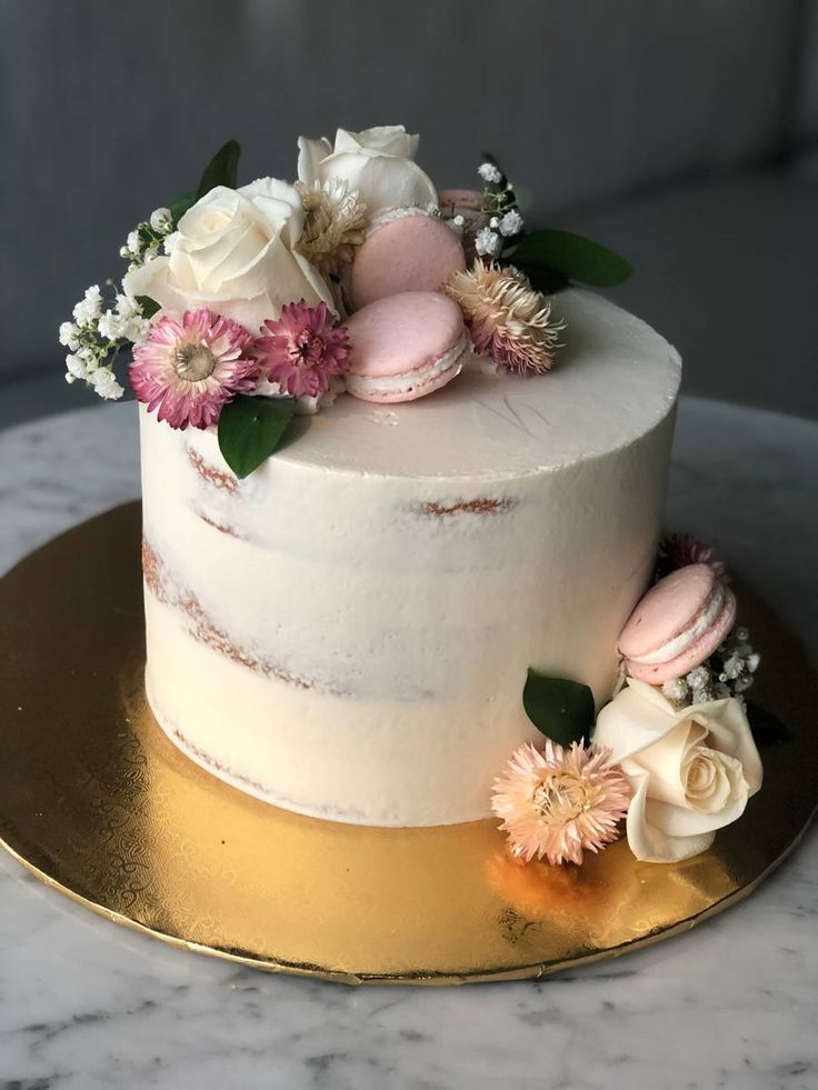 a white cake with pink and white flowers on top sitting on a gold platter