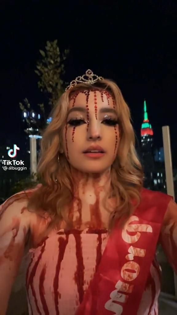 a woman with makeup and blood on her face is standing in front of a cityscape