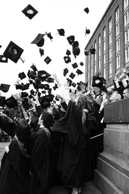 black and white photograph of graduates throwing their caps in the air at graduation ceremony on campus