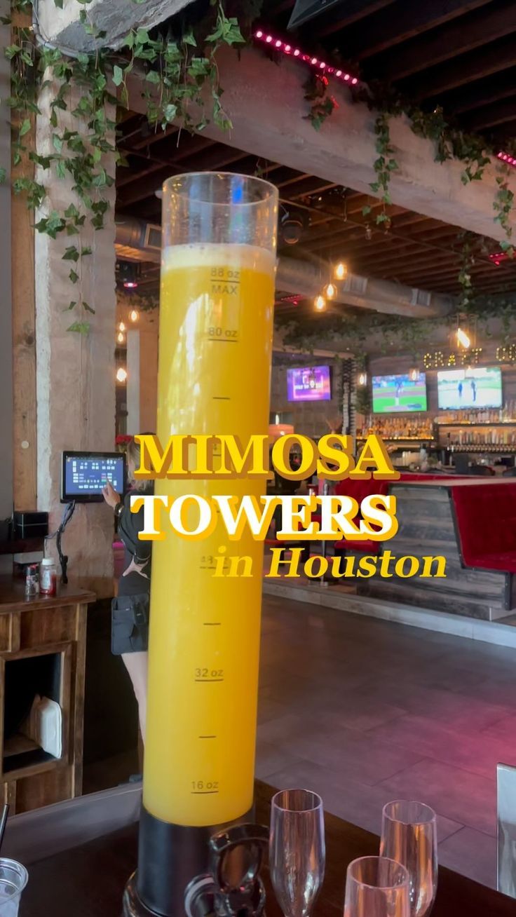 a tall glass filled with yellow liquid sitting on top of a table next to wine glasses