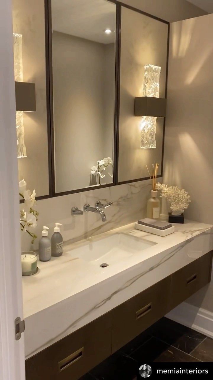 a bathroom sink with two mirrors above it and flowers in the vase on the counter