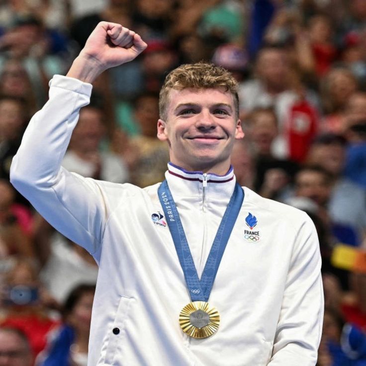 a man holding up his gold medal in front of a crowd