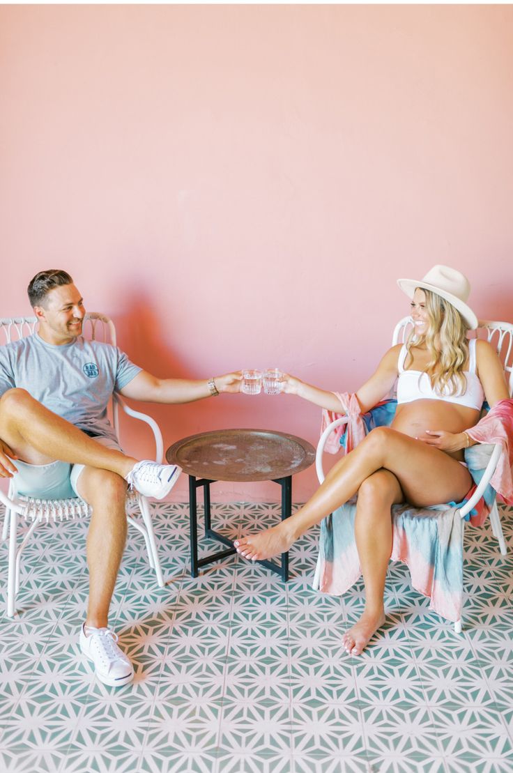 a man and woman sitting at a table in front of a pink wall with chairs