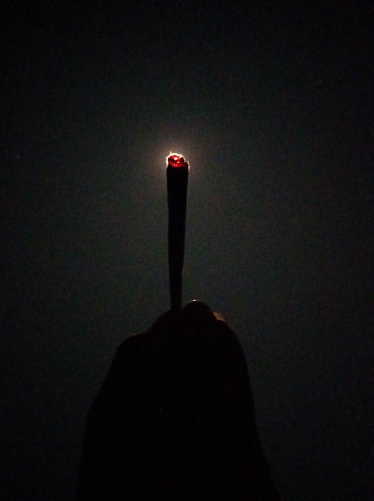 a person's hand holding up a lit candle in the dark with their fingers