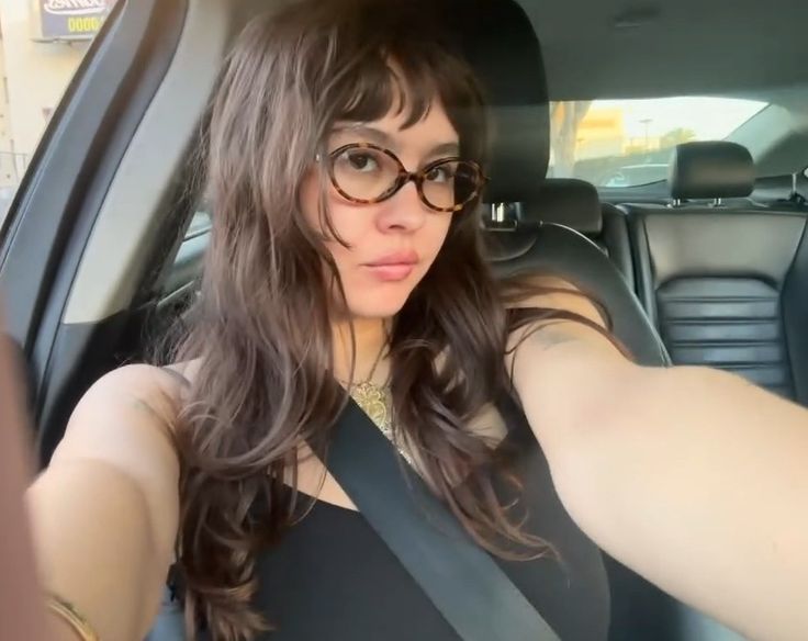 a woman wearing glasses sitting in the back seat of a car with her arm up