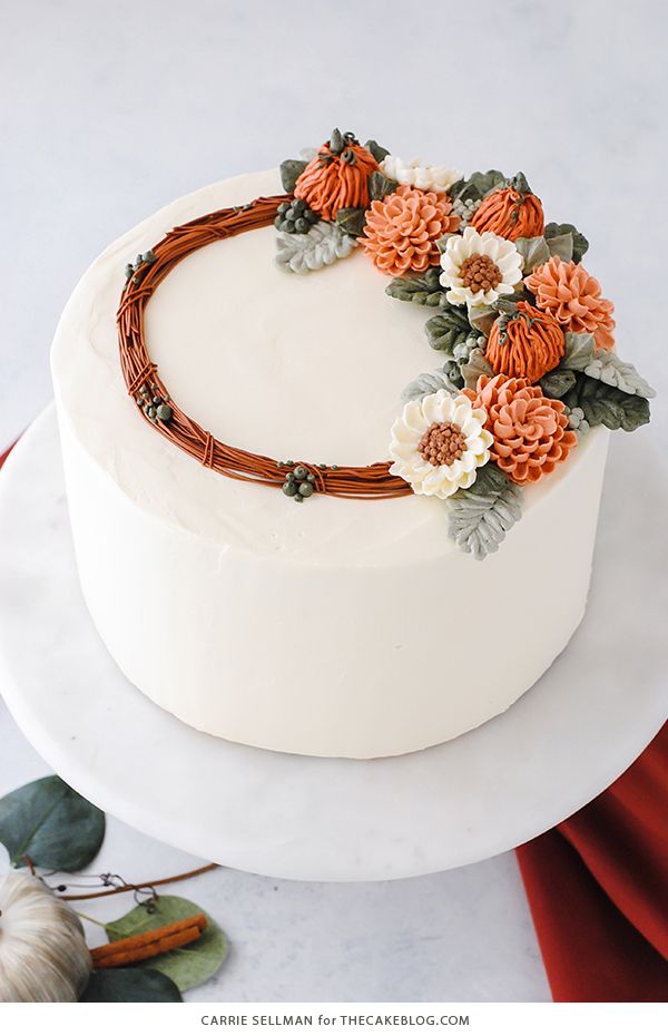 a cake decorated with flowers and leaves on a white platter next to pumpkins