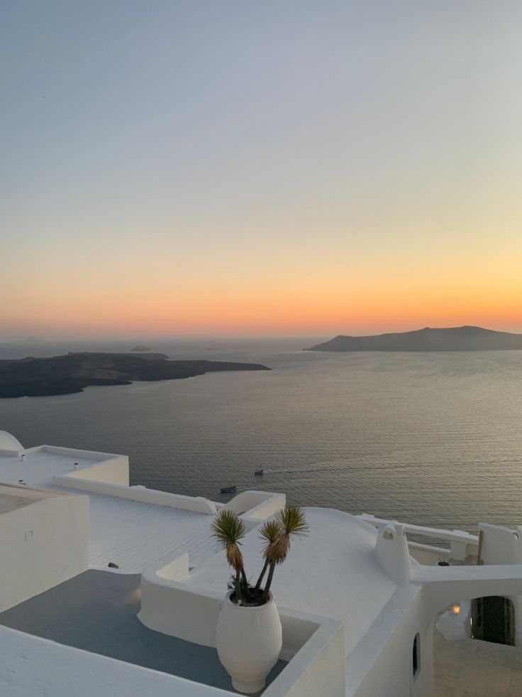 the sun is setting over an ocean with white buildings and palm trees in front of it