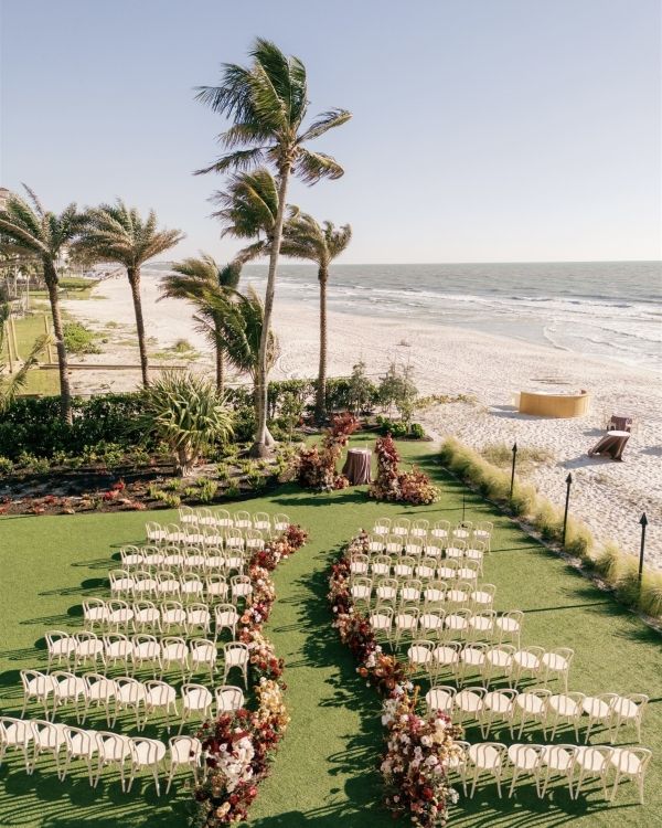 an outdoor ceremony set up on the beach with white chairs and flowers in the middle