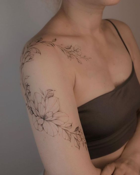 a woman with a flower tattoo on her arm and shoulder, looking at the camera