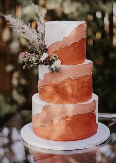 a three tiered wedding cake with pink and white frosting on a glass table