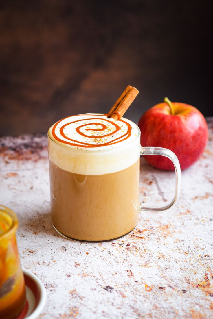 an apple cider with cinnamon in it next to two apples