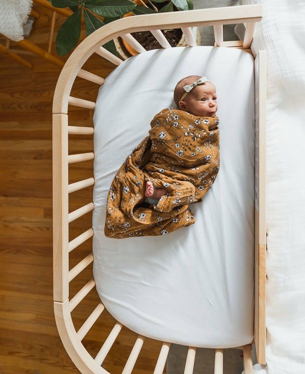 a baby wrapped in a blanket laying on top of a crib next to a potted plant