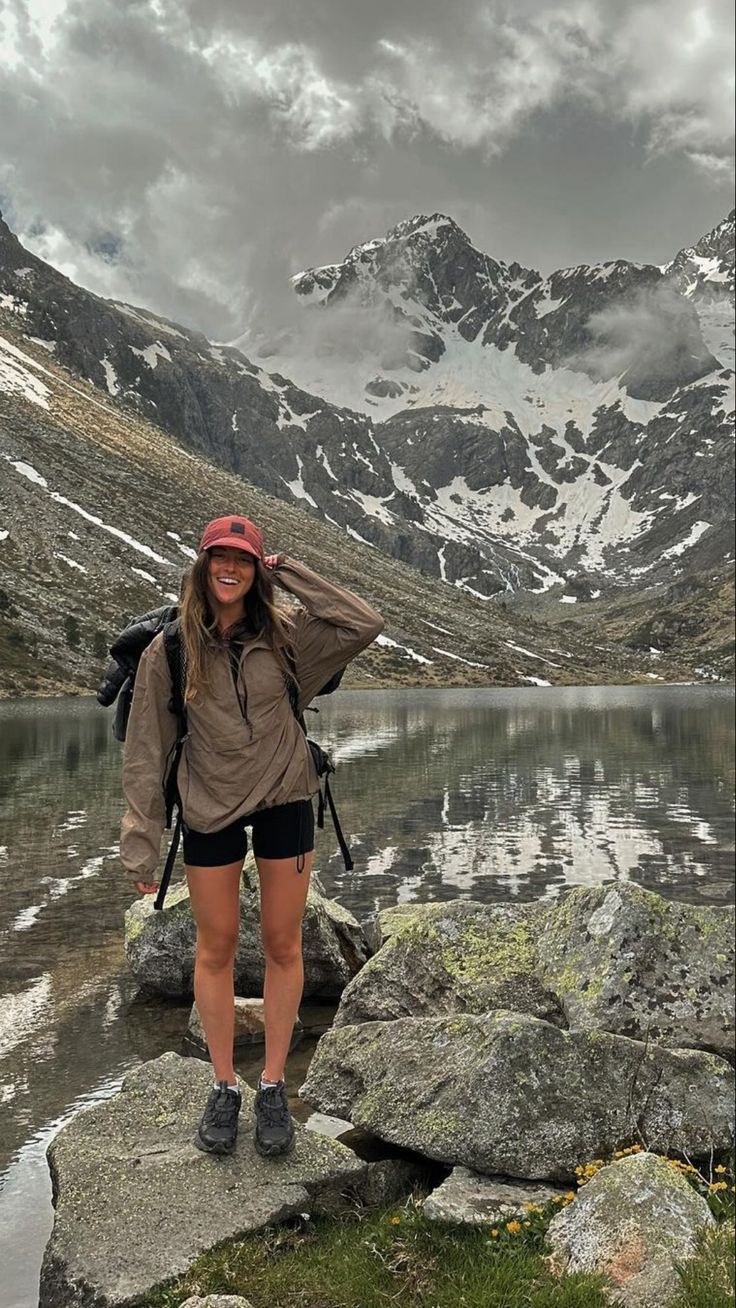 a woman standing on top of a rock next to a lake