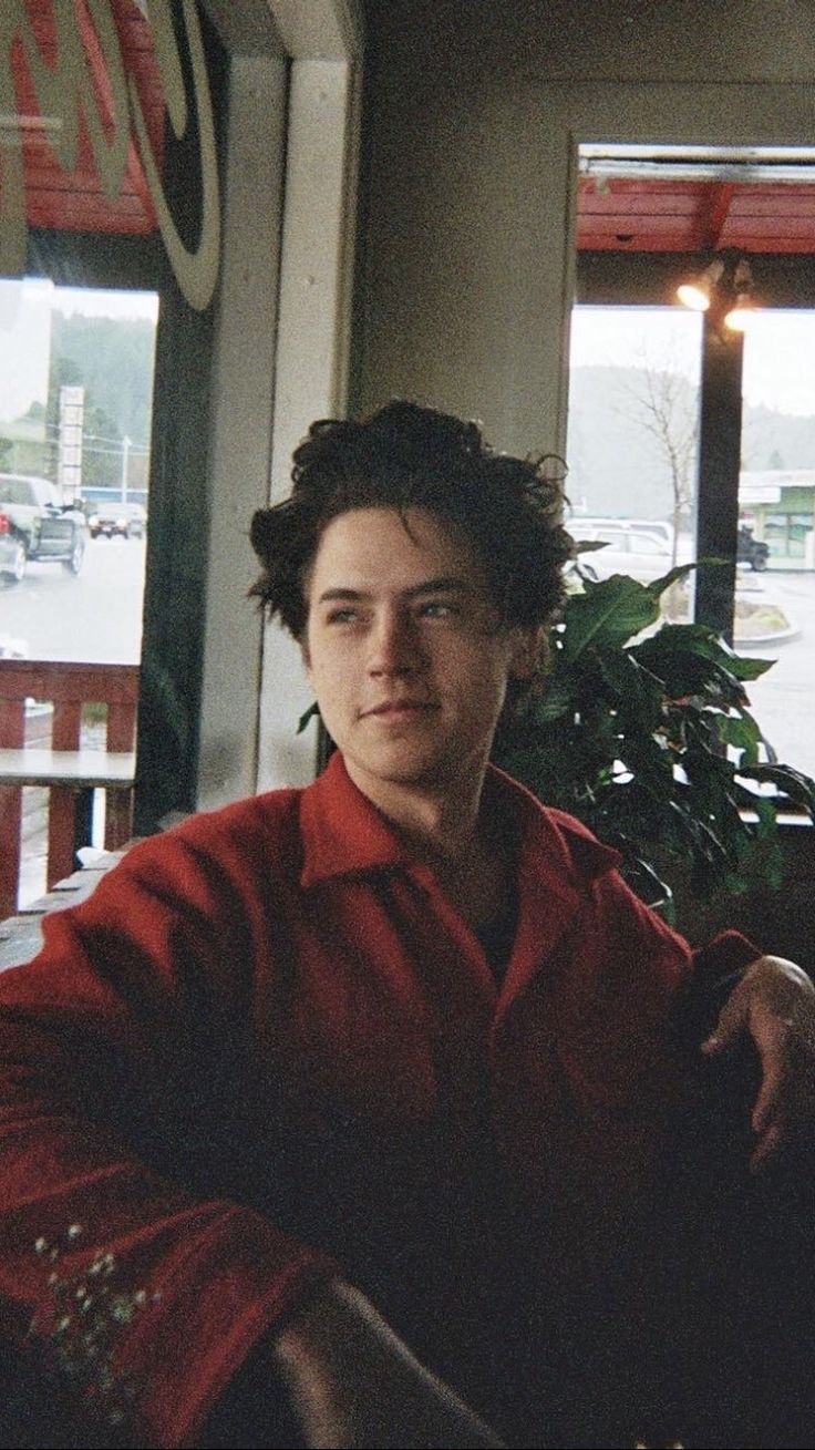 a young man sitting at a table in front of a window with his arms crossed