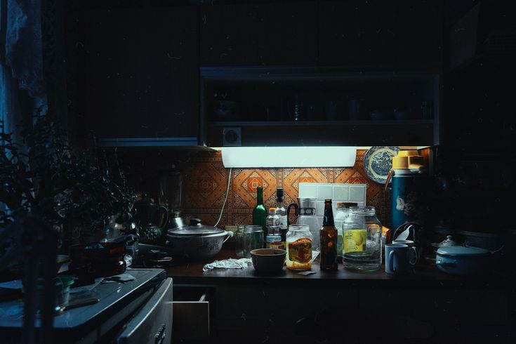 the kitchen counter is cluttered with bottles and other items, including an oven hood