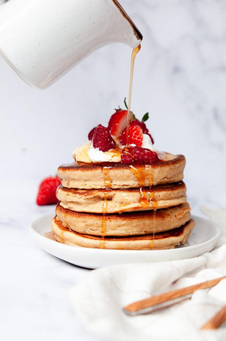 a stack of pancakes with syrup being drizzled over them and topped with strawberries