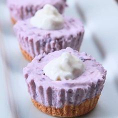 three cupcakes with purple frosting and whipped cream