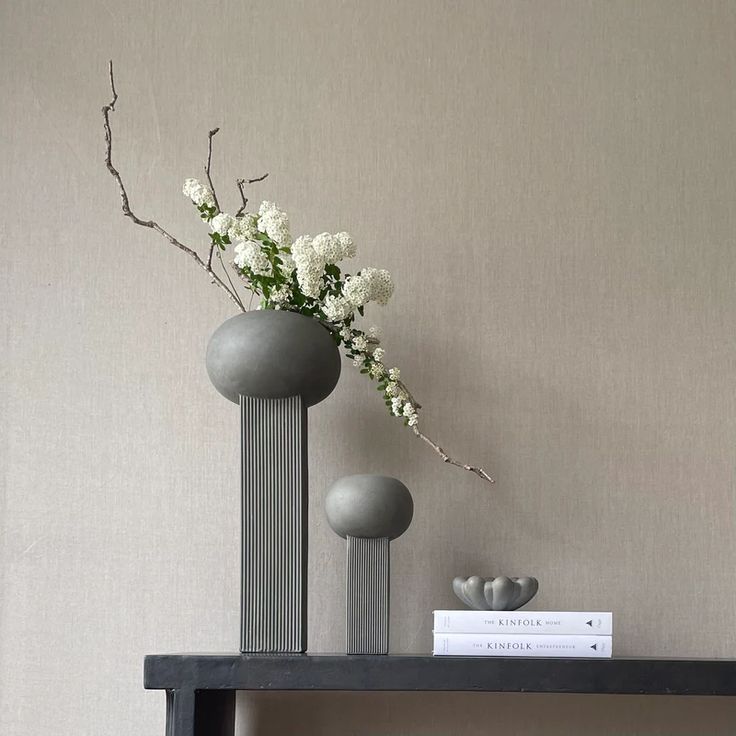 two vases with white flowers are sitting on a shelf in front of a wall