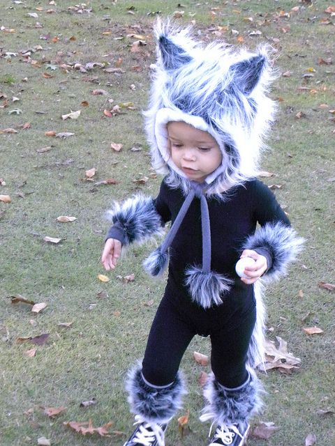 a small child in a costume walking on the grass with leaves all over it's feet