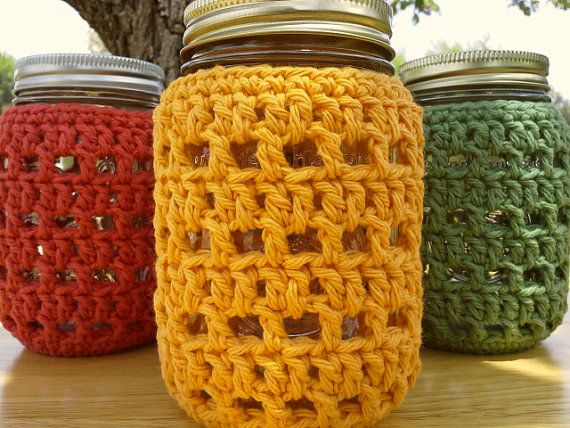 crocheted mason jars lined up on a table next to a tree in the background