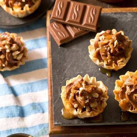 mini desserts with chocolate, nuts and caramel on a black tray next to a striped towel