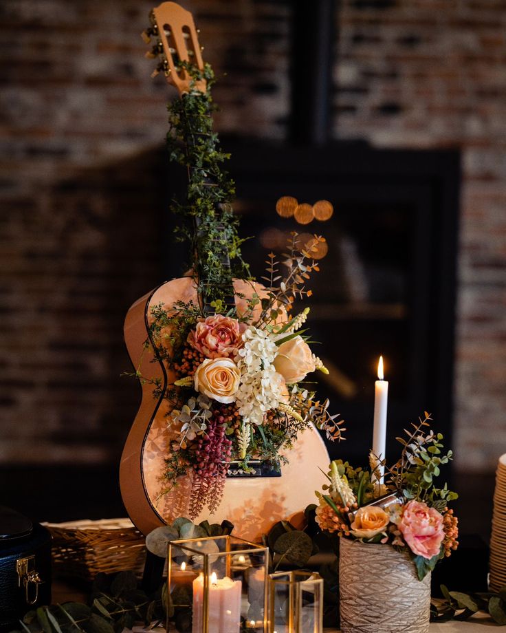 an arrangement of flowers and candles on a table in front of a fireplace with a guitar