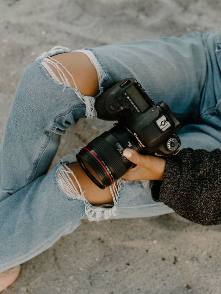 a person sitting on the ground holding two camera's hands up to their sides