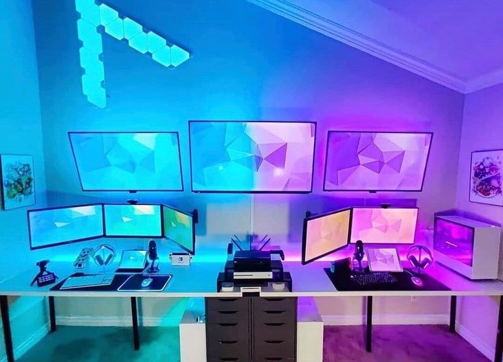 there are many computer screens on the desk in this room with purple lights and blue lighting