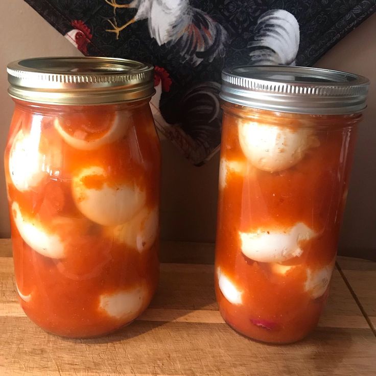 two jars filled with food sitting on top of a wooden table next to a rooster