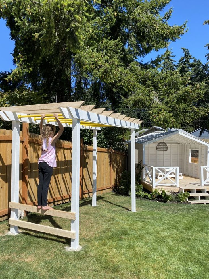 a woman standing on top of a wooden bench under a pergolated roof next to a shed