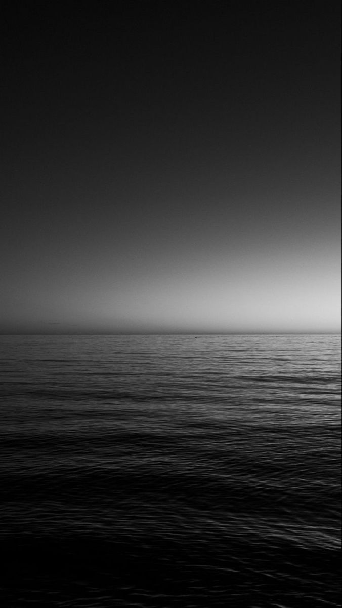 a black and white photo of the ocean at night with only one boat in it