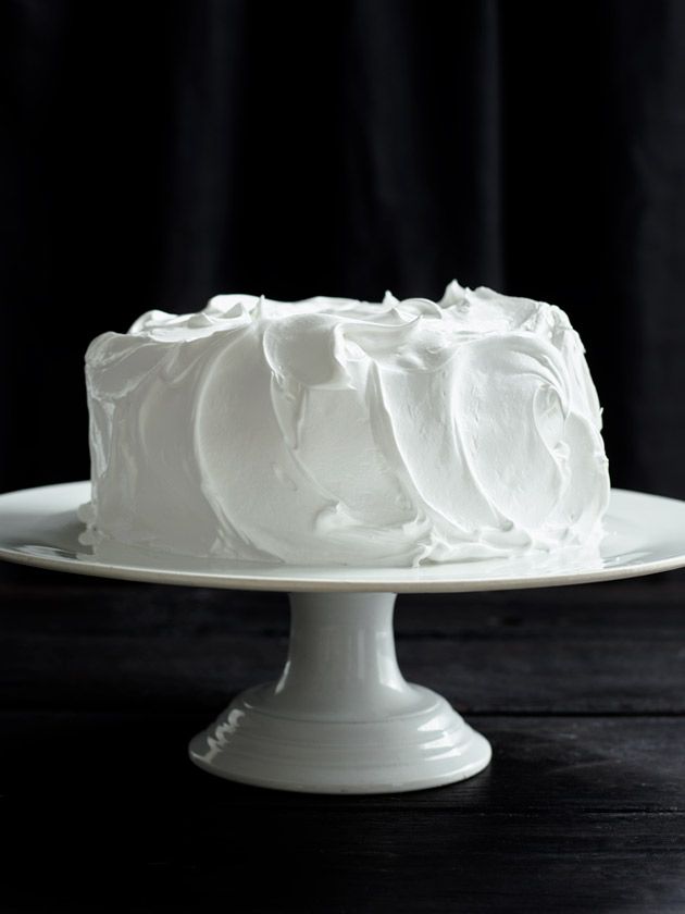 a white frosted cake sitting on top of a white cake plate with black background