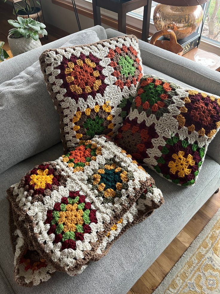 two crocheted pillows sitting on top of a gray couch next to a window