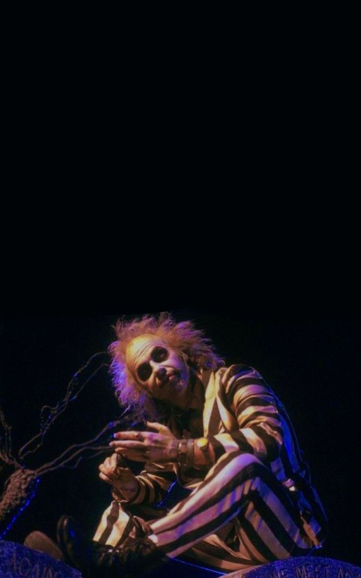 a man in striped pants sitting on top of a stage with his hands clasped to his chest