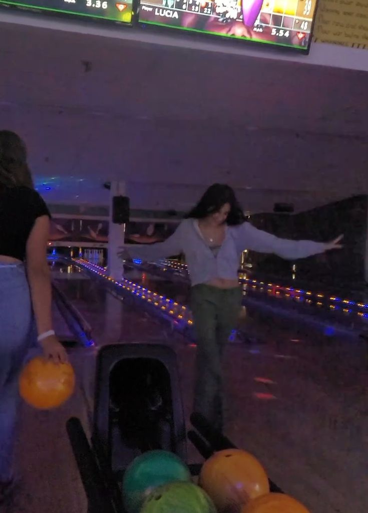 two women are playing bowling in an indoor bowling alley with neon lights on the ceiling