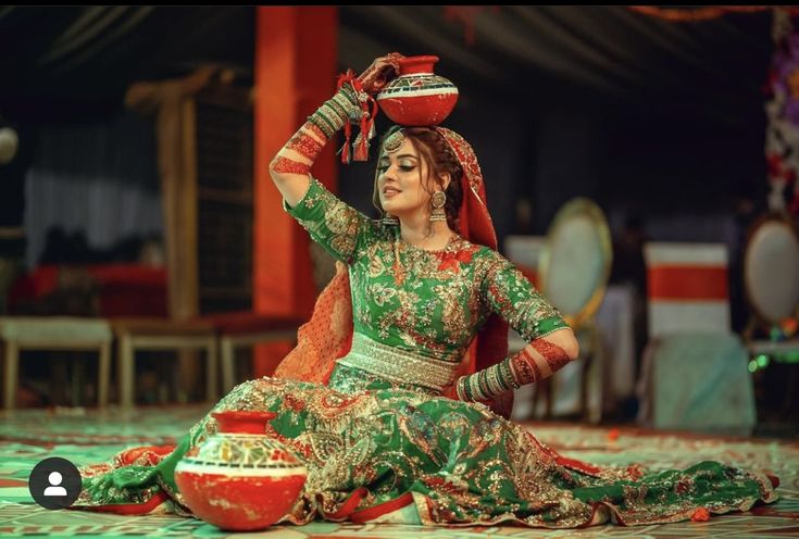 a woman sitting on the ground in a green and red dress with her hands up