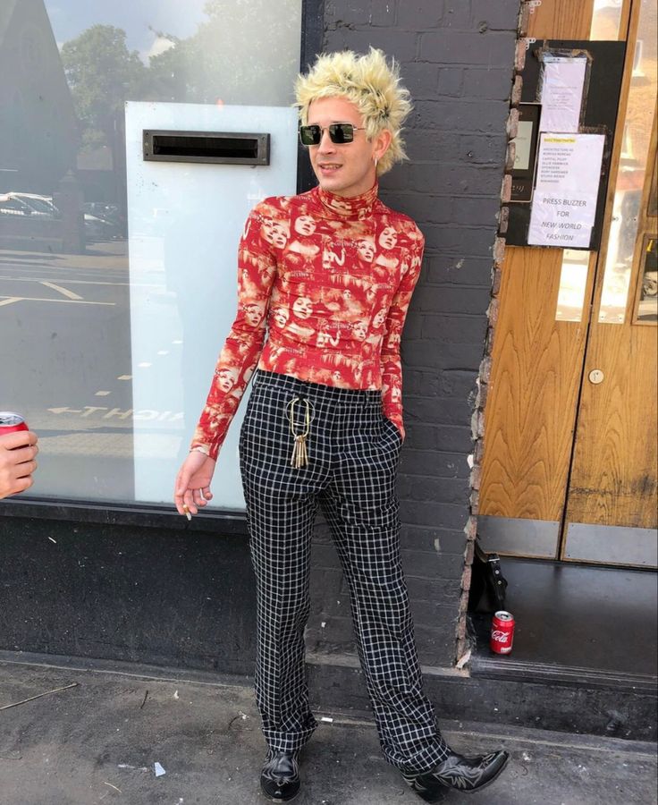 a woman with blonde hair and sunglasses standing in front of a building wearing plaid pants