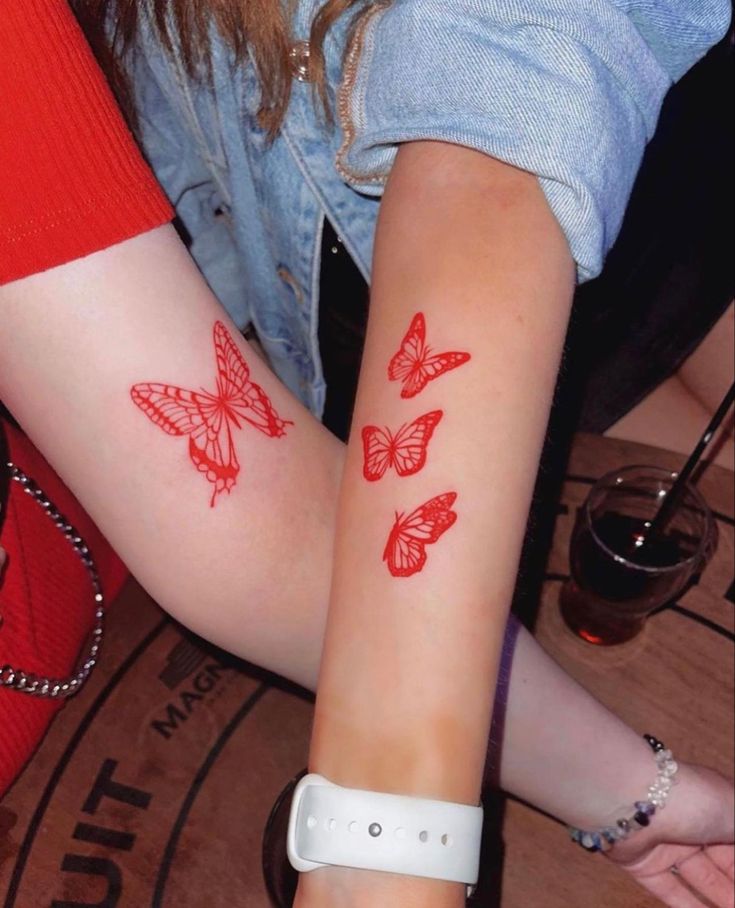 two girls with tattoos on their arms and one has red butterflies on her left arm