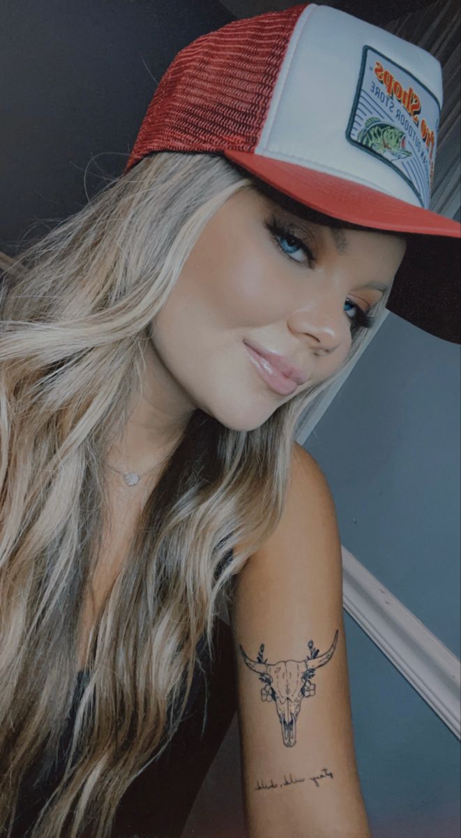 a woman with long hair wearing a red and white trucker hat is looking at the camera