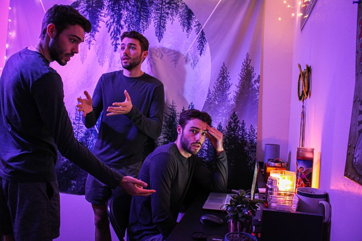 three men standing in a room with purple lighting and trees on the wall behind them