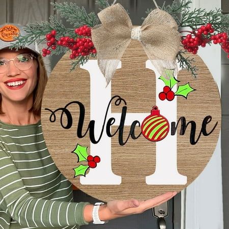 a woman holding up a wooden sign with the word welcome on it and holly wreaths