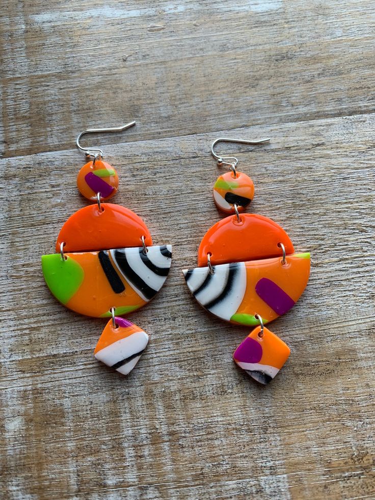 two orange and green earrings on top of a wooden table